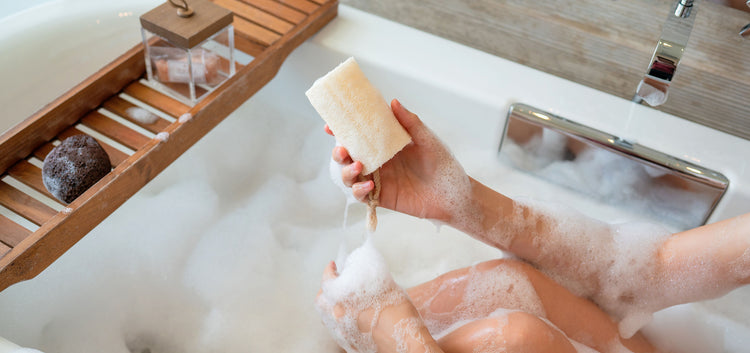 Woman enjoying a bubble bath while holding a natural loofah sponge, showcasing sustainable personal care in a cozy, spa-like bathroom